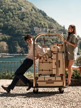 Young woman in a convertible car in front of Lake Como with a Trolley and a Legacy Bag from the Bellagio collection in Cream color. | Bric's Milano